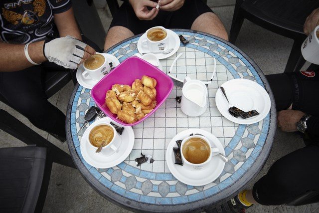 A round table set with coffee and cake. People can be partially seen sitting around the table.