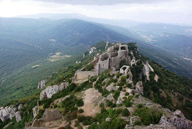 An arial view of castle ruins atop a tall hill. Hills stretch away into the background.