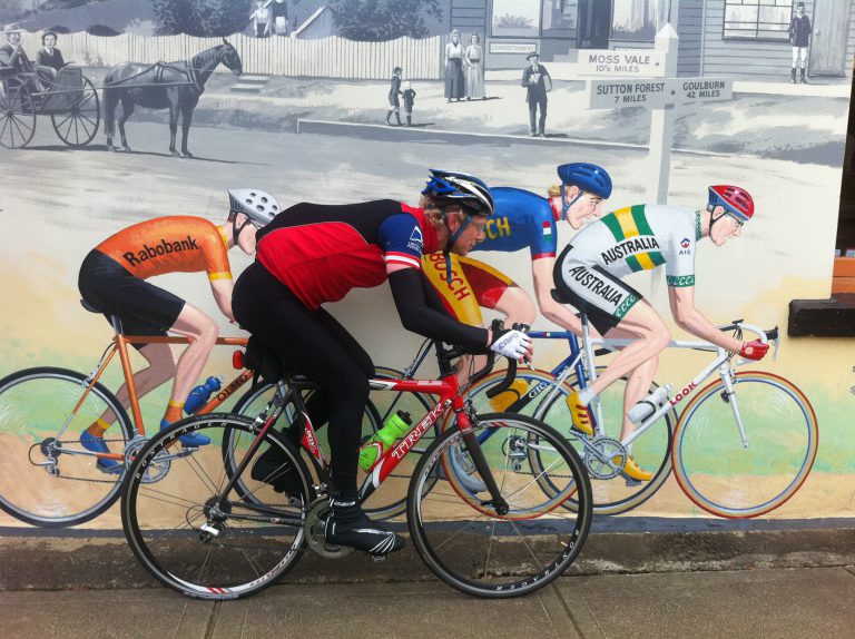A bike rider cycling past a mural of cyclists.