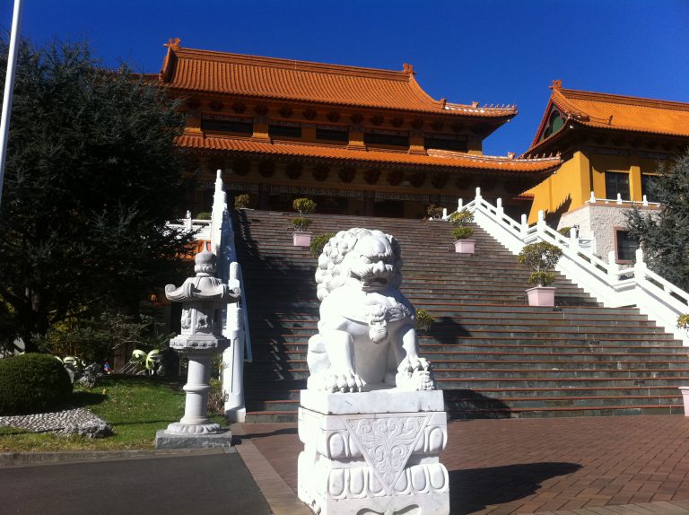 A traditional Asian temple with steps leading up to the temple. White statues line the steps.