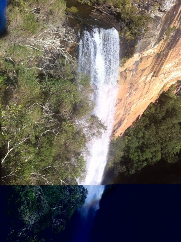 View of a waterfall cascading over a steep sandstone cliff, from above.