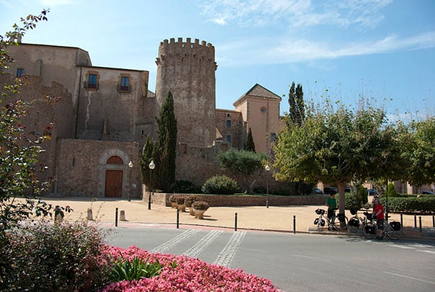 An old walled village from outside, across the square. Part of the wall includes a tower.