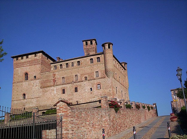 An old town castle sits atop a hill. There is a brick wall running along the road that leads up past the castle.
