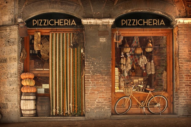 A shopfront in an old town. Two windows with displays of cured meats.