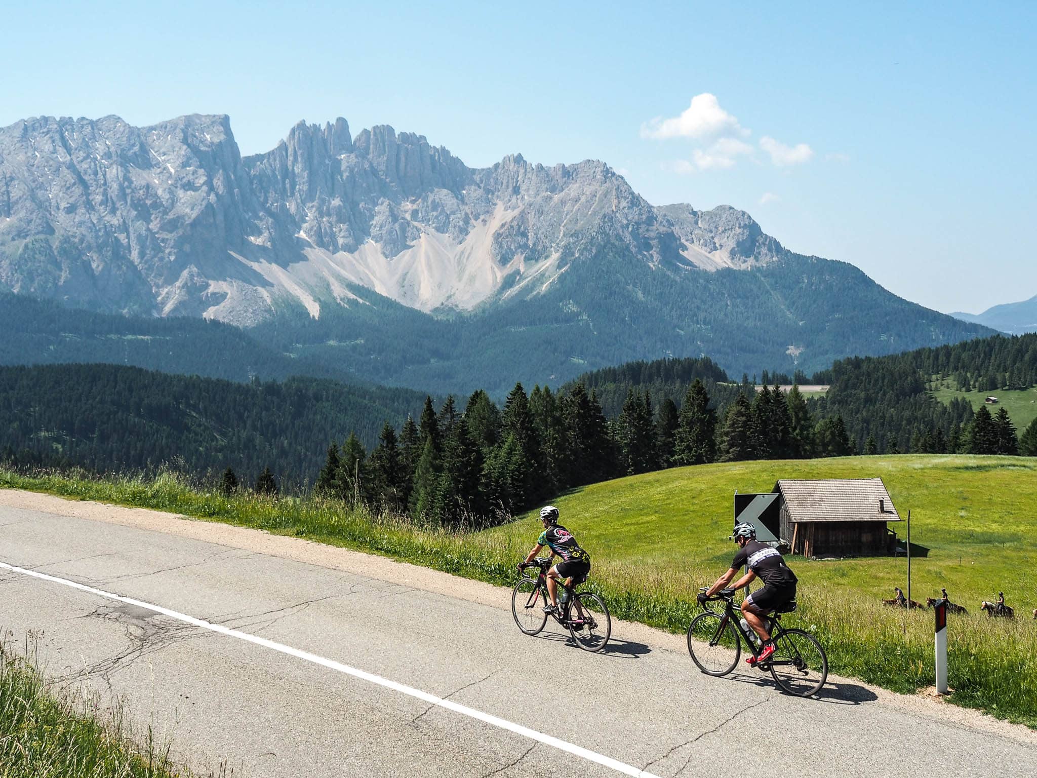 Two cyclists riding along a road through the Dolomites with a view of mountains in the background