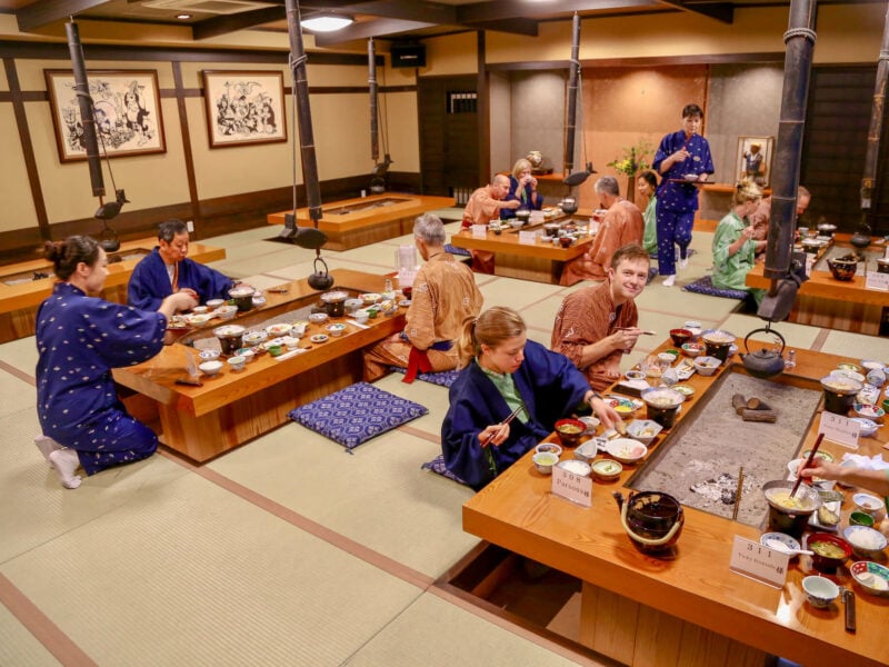 Ride and Seek guests seated on the floor around four separate tables in a Japanese eating house in traditional Japanese dress. The tables where the guests are seated are laid with many bowls of various Japanese dishes.