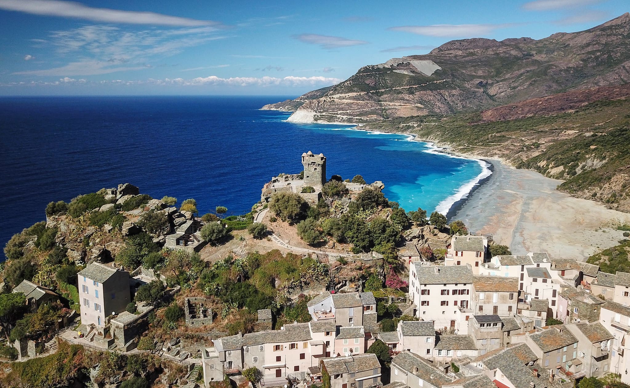 An old town sits atop a hill with a very blue coast in the background.