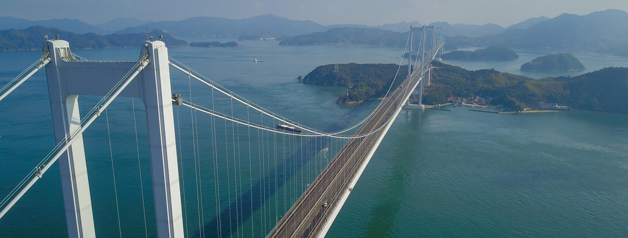 An aerial view of a huge bridge spanning an expanse of water, using a peninsula as a foundation midpoint.