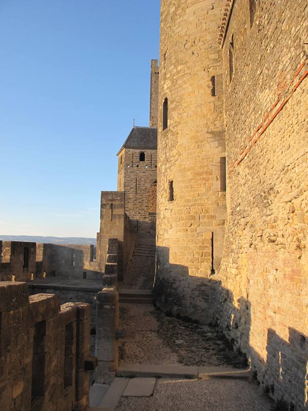 A wide pedestrian path flanked by the very tall walls of an old castle.