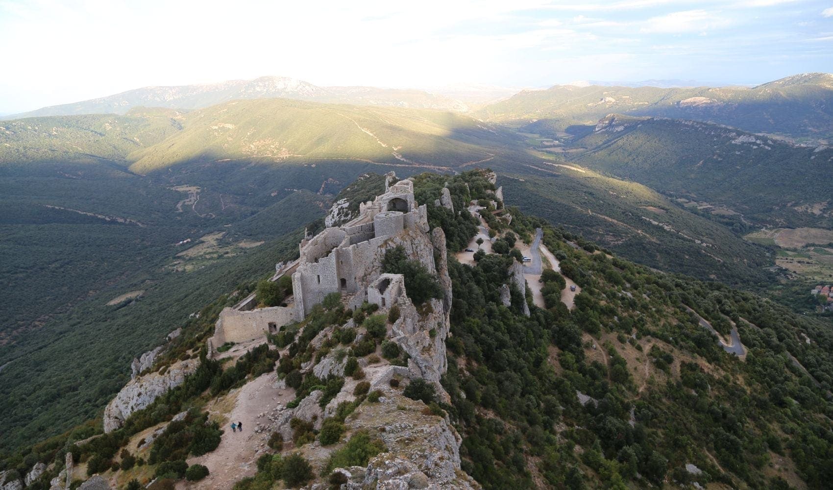 The ruins of an old castle perched atop a stony ridge with hills in the background.