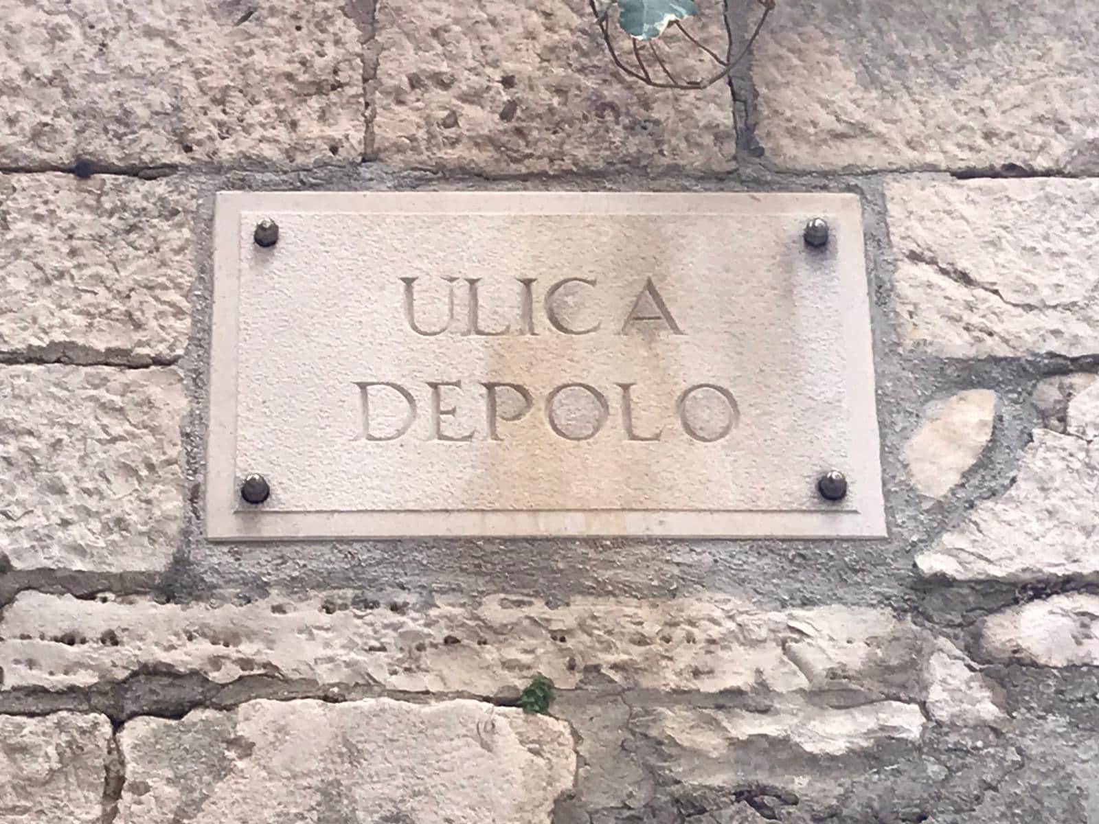 A plaque in a foreign language is bolted onto a stone wall.