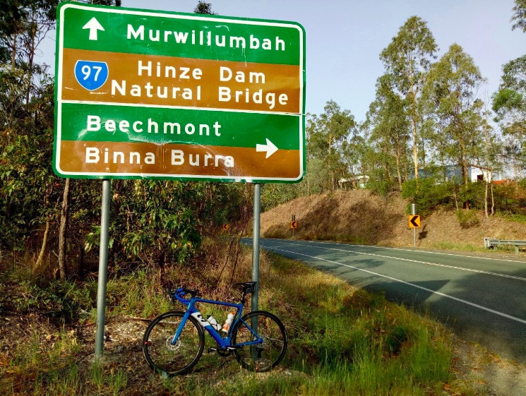 Michael's road bike leans against a large highway road sign alongside the single-lane highway.