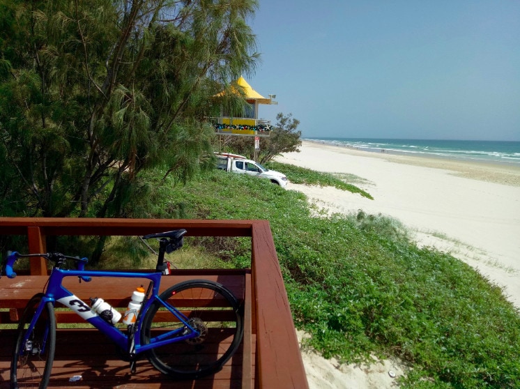 Michael's bike rests against the lookout railing overlooking the beach with a surf lifesaving structure in the background.