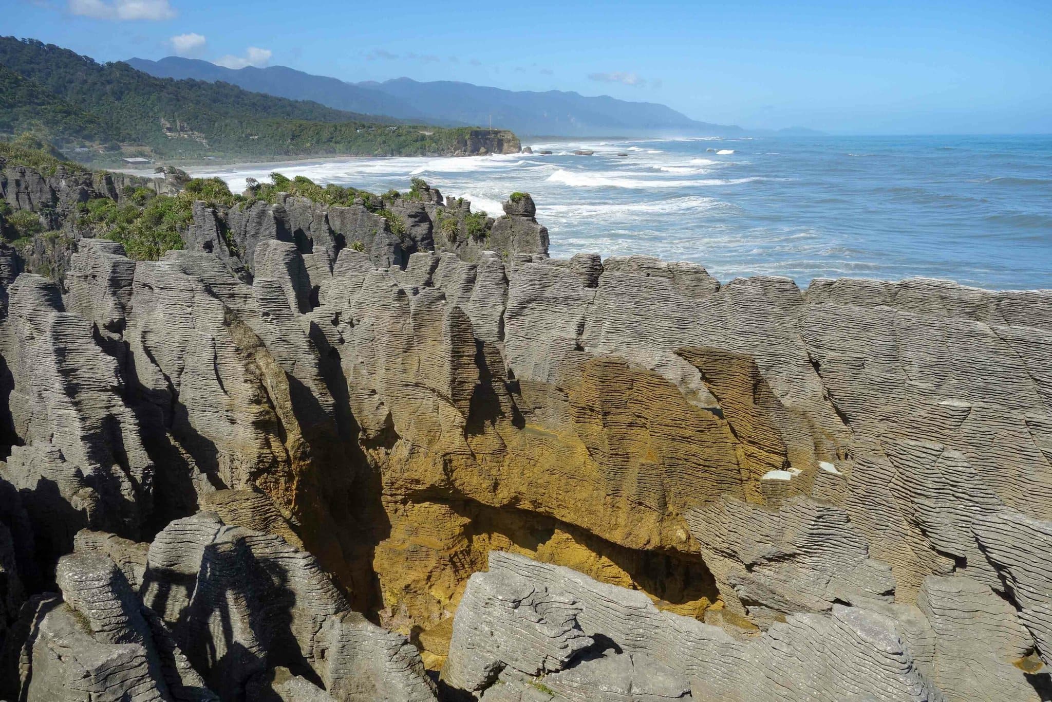 A photo looking south along New Zealand's South Island coastline with Pancake Rocks in the foreground.