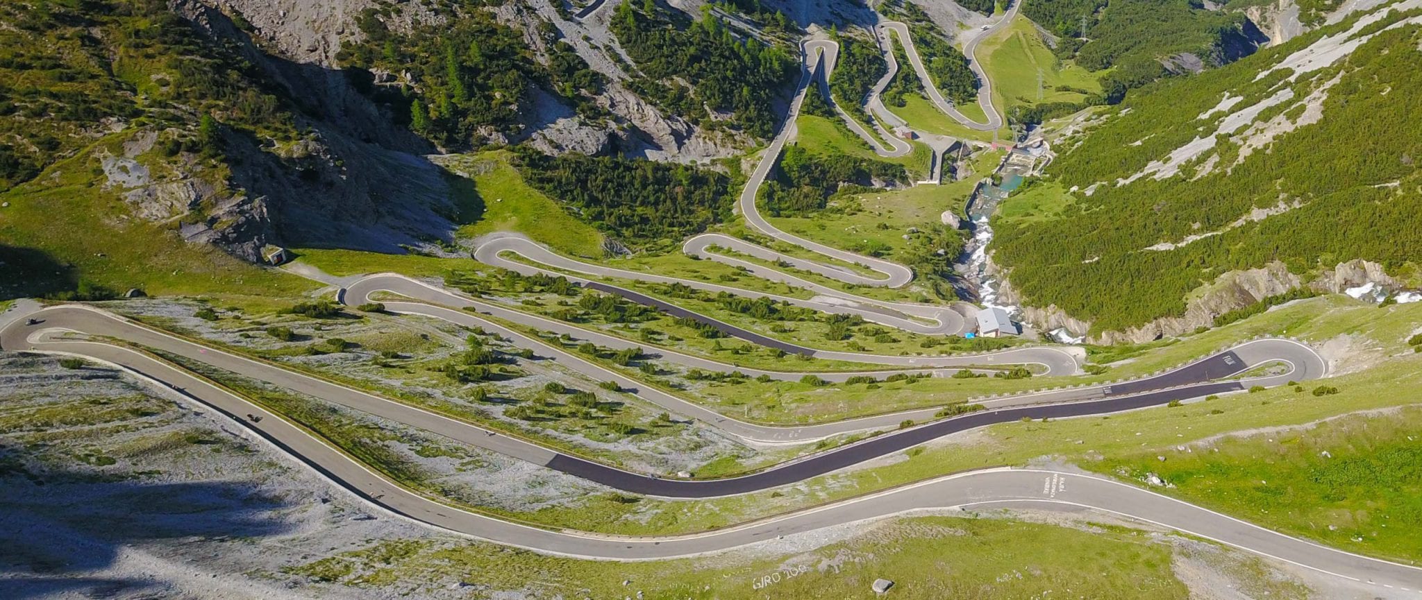 A road winds down a steep green valley, with 12 switchbacks visible.