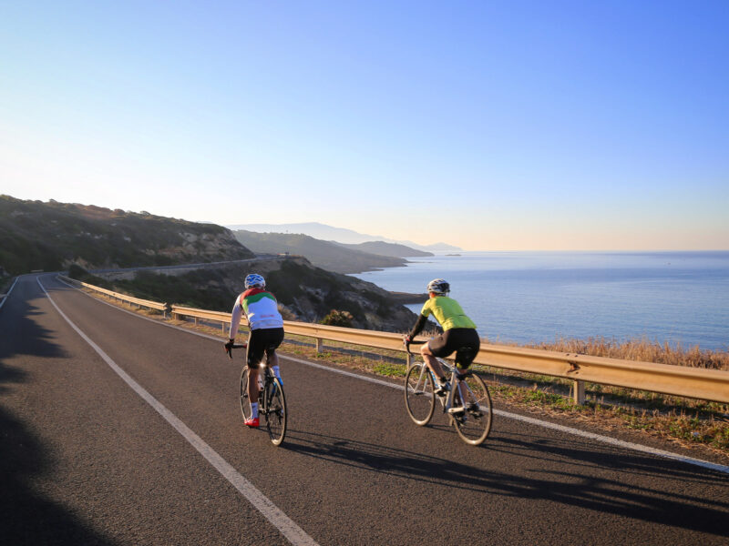 Cyclists on a Ride and Seek bike tour riding along a coastal road on a clear blue sky day.