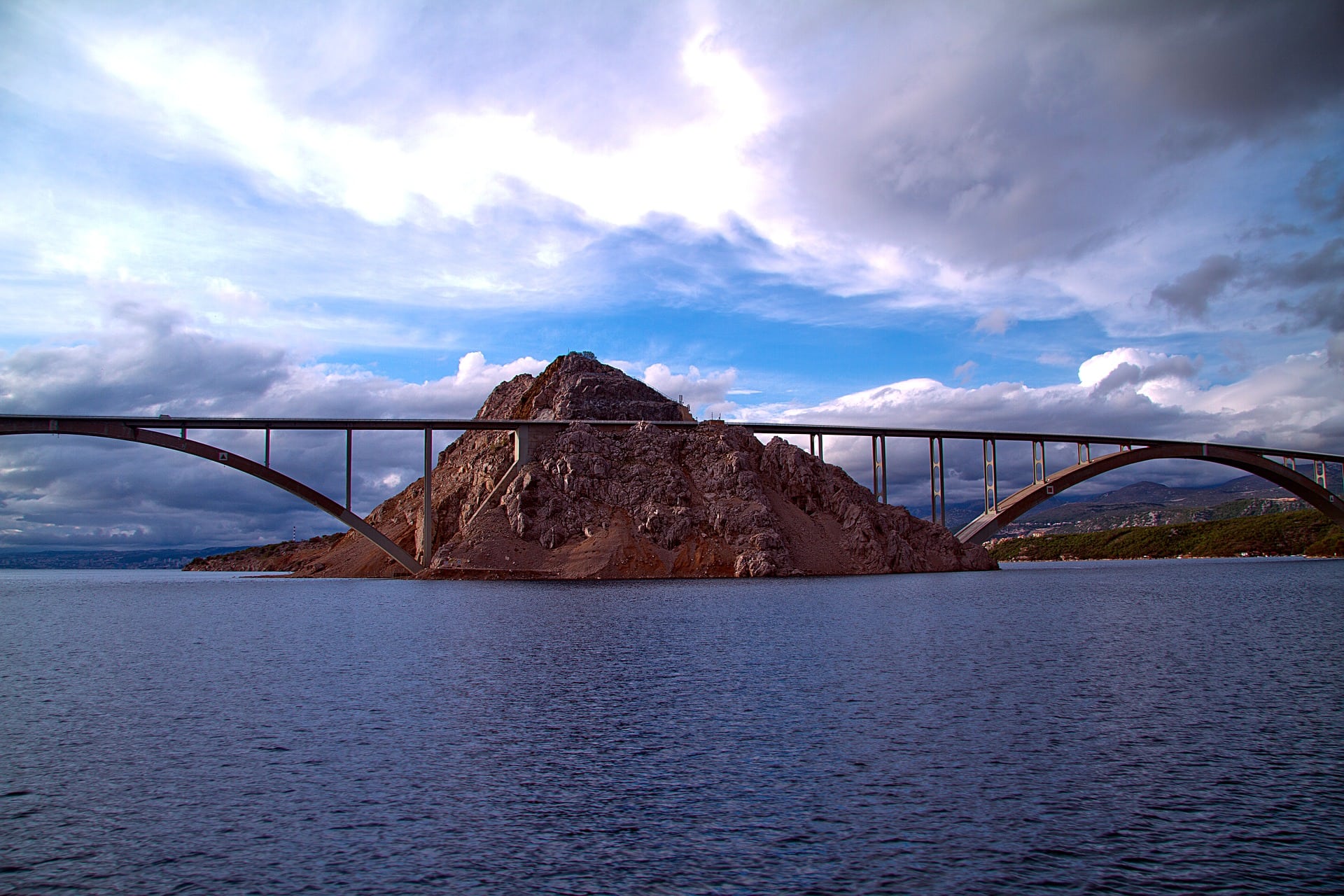 A tall, arched bridge spans an expanse of water, using a small island as a support for the bridge.