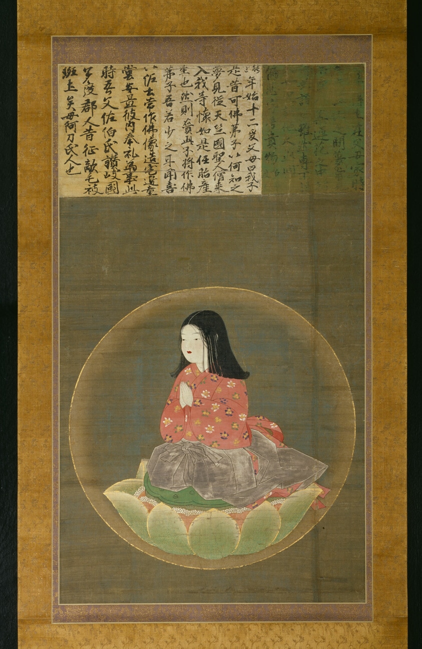 A photo of a wall hanging showing a portrait of a young boy sitting in a lotus leaf within a circle. There is Japanese lettering above the boy.