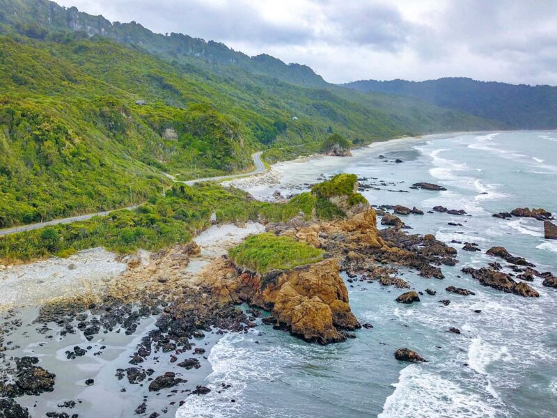 Road running along the ruggedly beautiful wild west coast of the south island with the ocean on one side and the mountains on the other