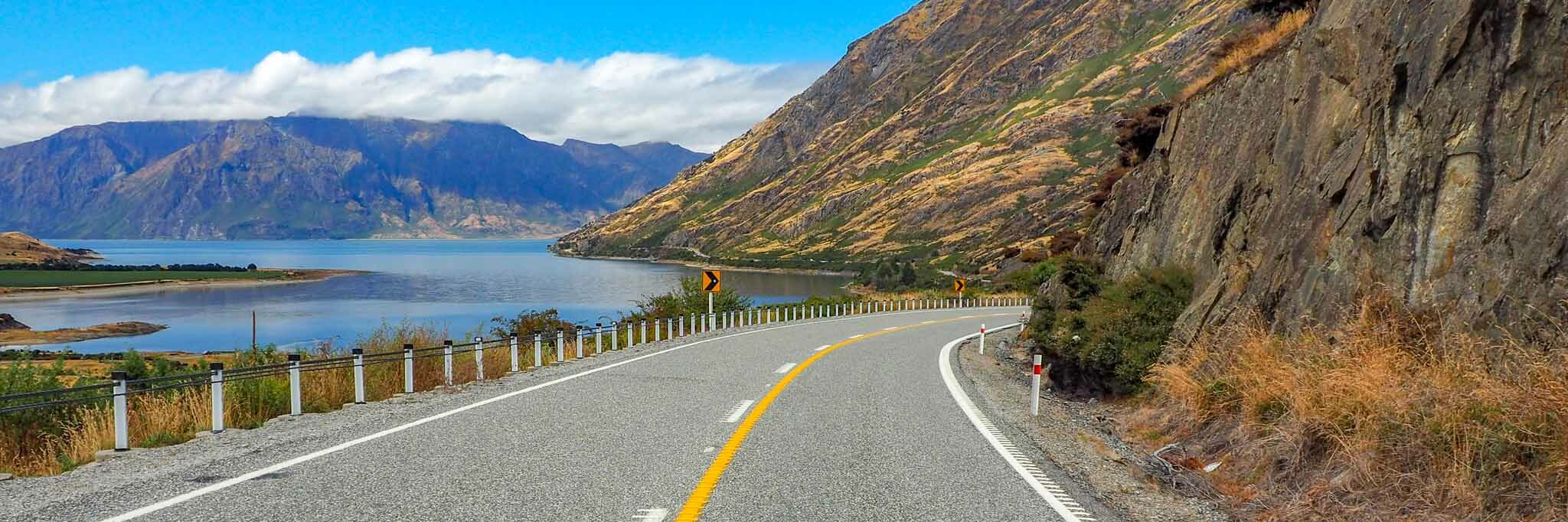 Road running along a lake with mountains in the back ground