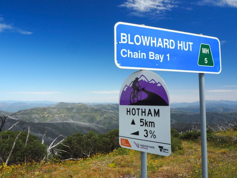 Alpine road signs along the top of the ridge to Hotham, showing gradient of 3% at Blowhard Hut on the Great Alpine Way, with mountain tops views extending away into the background