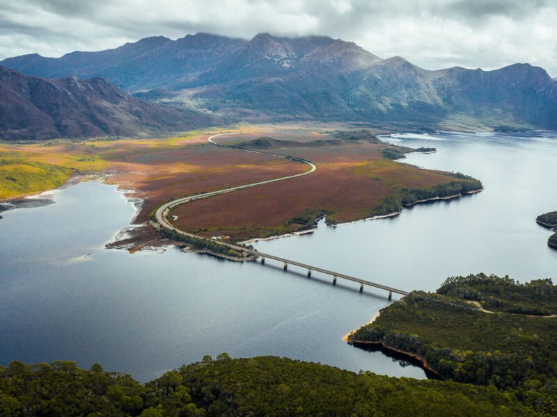 Bridge going across a lake with the road winding into the distant mountains in the western Tasmanian wilderness.