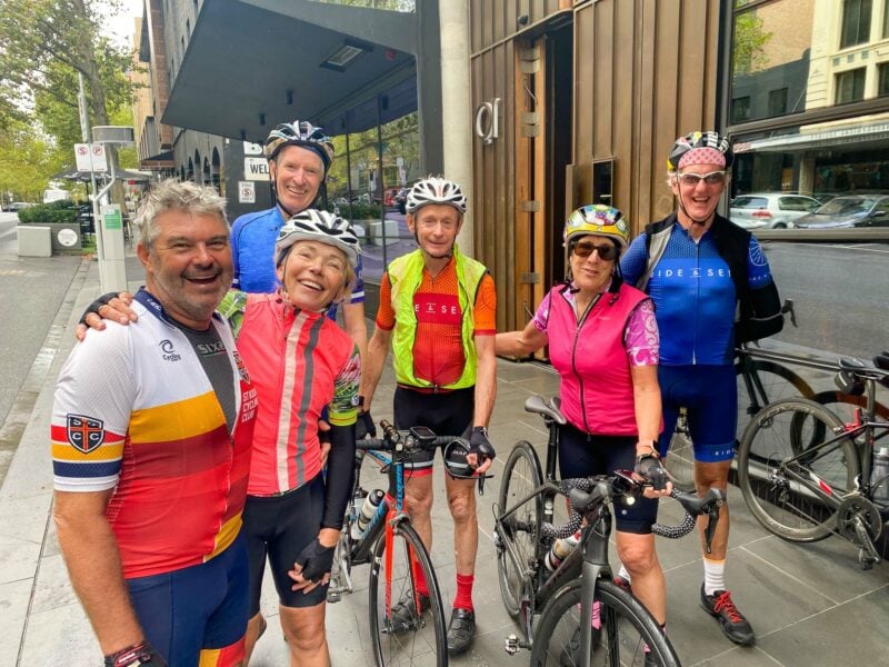 Tour guests in a relaxed group photo holding their bikes on Russel Street Melbourne, outside the QT Melbourne accommodation