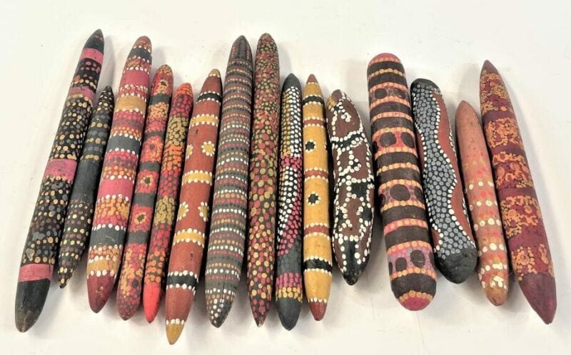 A range of traditional message sticks that laying side by side. The message sticks are long thin pieces of timber painted with traditional artwork in various colours.