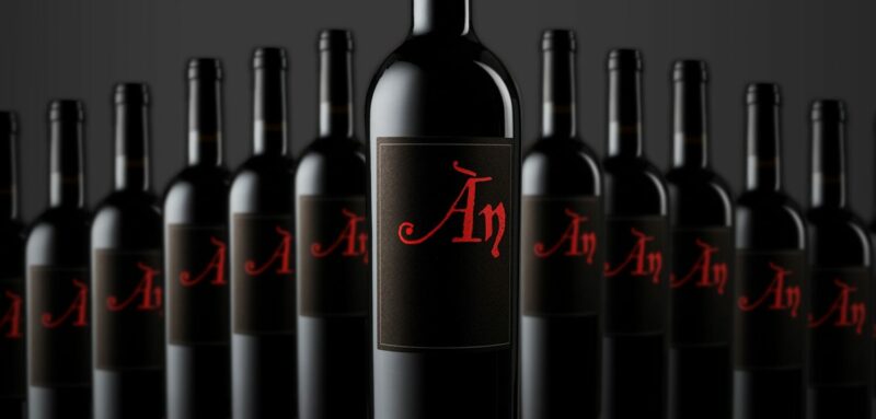 A row of black wine bottles. The labels are also black, with red writing.