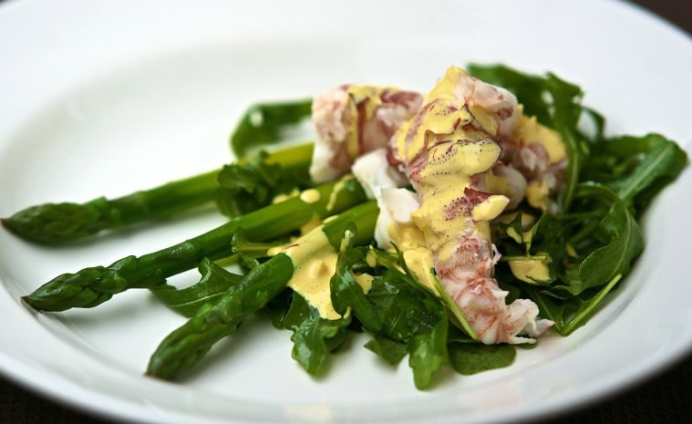 A plate of Morton Bay Bugs sits on a bed of green asparagus and rocket, drizzled with a creamy aioli sauce.