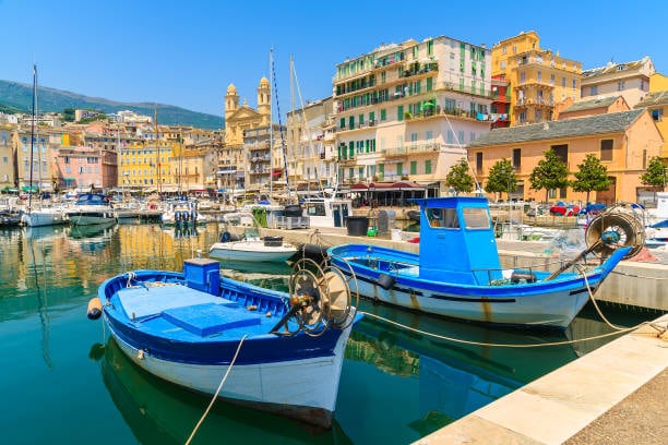 An old town fills the background overlooking the harbour. There are traditional fishing boats on the still waters of the harbour in the foreground.