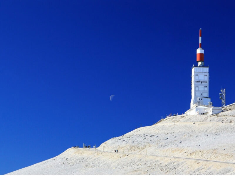 A tower sits on a snow covered mountain top with a clear blue sky in the background.