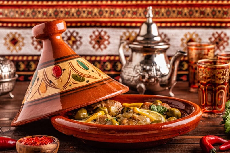 A tangine with the lid ajar revealing a dish of traditional Moroccan food.