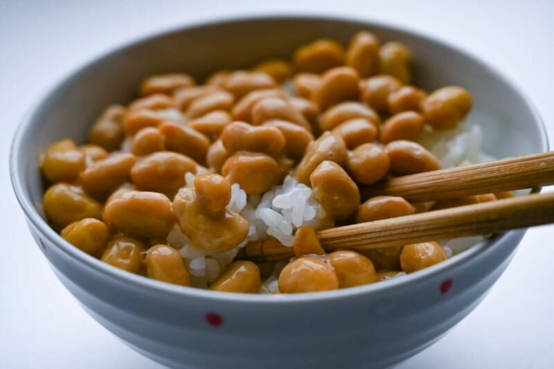 A bowl of Natto with a pair of chopsticks resting in the bowl.