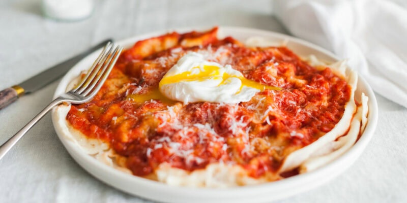 A plate of traditional Italian food sits on a table set with a white table cloth and some cutlery.