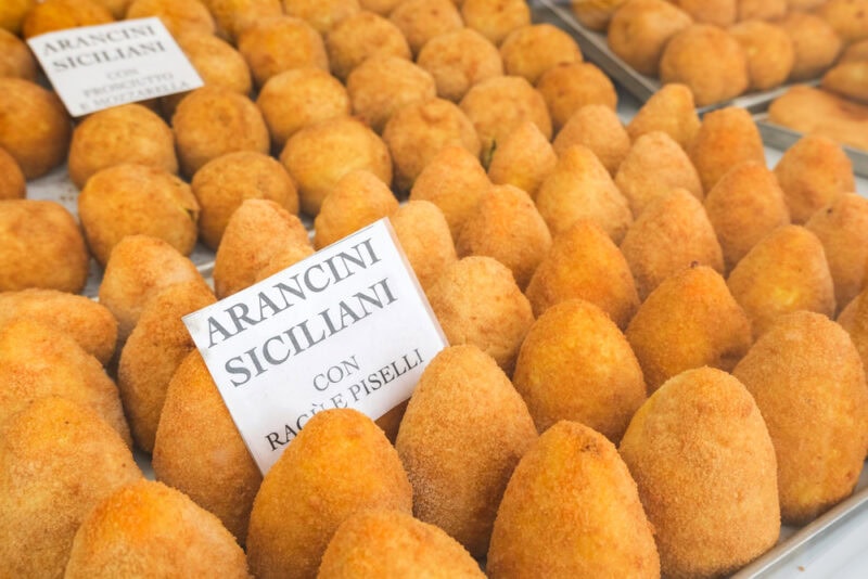 Close up photo of arancini for sale, displayed in neat rows.
