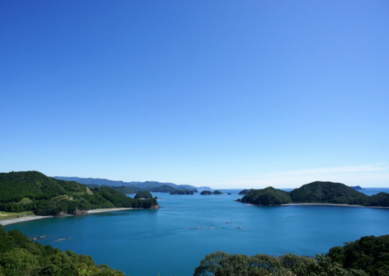 A large lake surrounded by low hills and a clear blue sky above.
