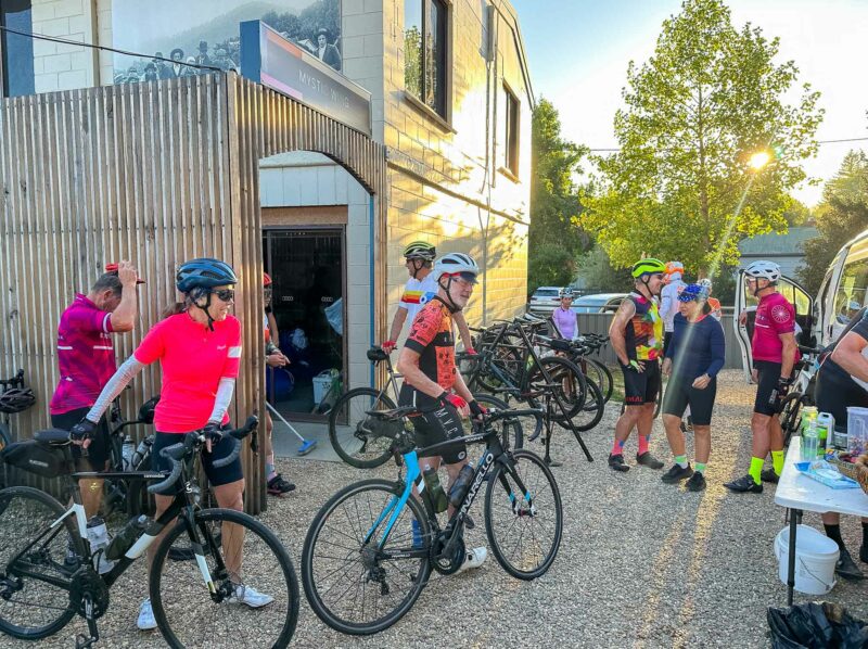Group of cyclists gathering with their bikes outside a building at Bright Velo in the morning sunlight, preparing for the day's ride.