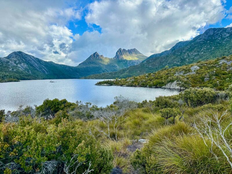 Scenic view of a lake surrounded by mountains, with Cradle Mountain rising under a partly cloudy sky