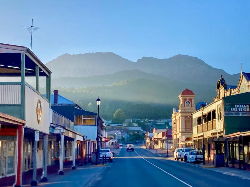 Wide, quiet Queenstown street lined with historic buildings, with misty mountains in the background at sunrise.