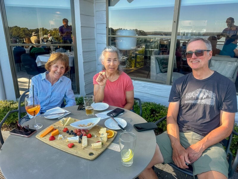 Three guests enjoying cheese and drinks at an outdoor restaurant table at Strahan Village on a sunny day.