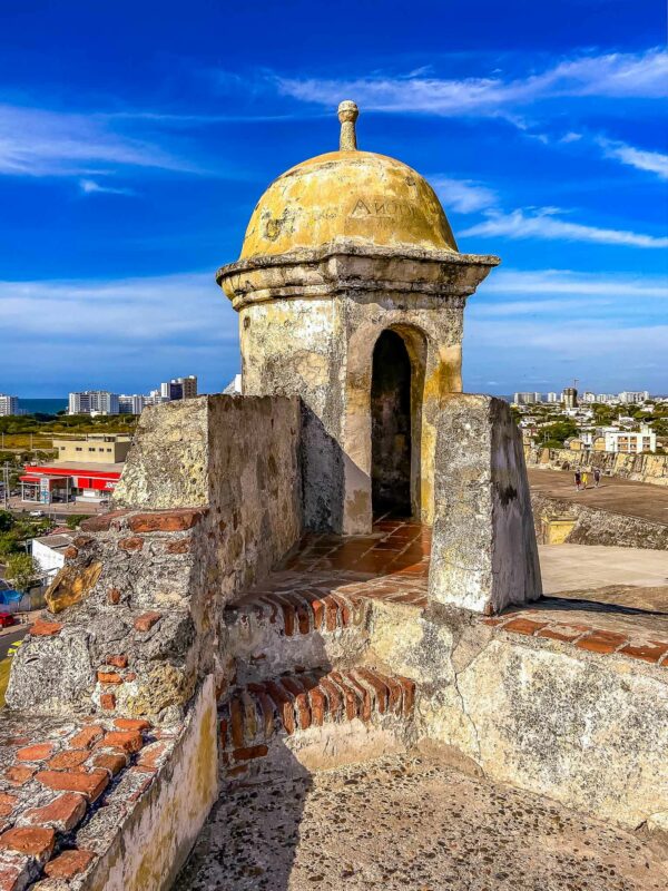 Historic stone sentry tower on Cartagena’s colonial fortress stands against a vivid blue sky, with a rounded dome and brick steps