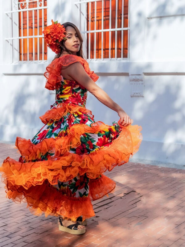 Traditional dancer twirling in a vibrant orange folkloric dress with floral headpiece.