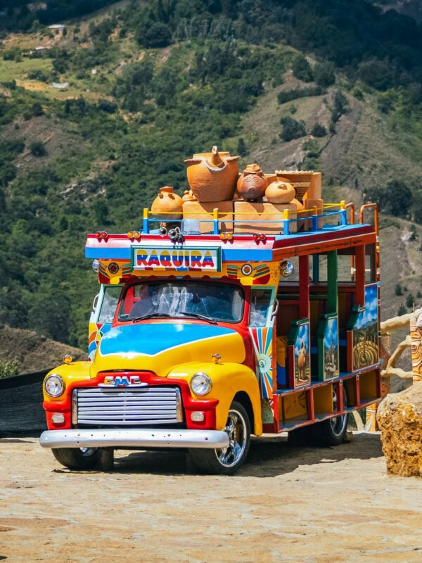 Brightly painted traditional Colombian chiva bus in Ráquira, topped with clay pottery, set against a mountain backdrop