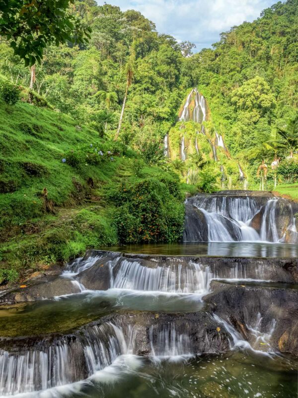 Tiered waterfalls flowing through lush green forest into natural pools.