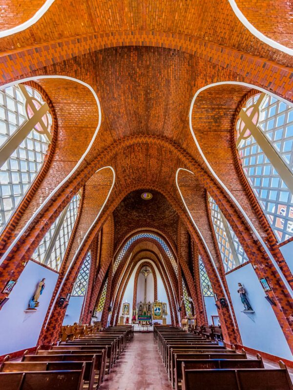 Wide view of a Colombian church interior with tall red-brick arches, stained glass walls, and wooden pews.
