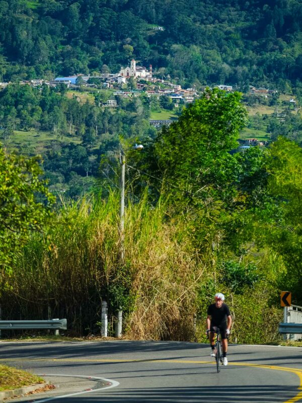 Cyclist riding uphill on a winding rural road with a small mountain town and white church visible in the distance.