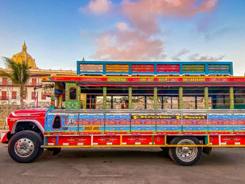 Traditional Colombian chiva bus painted in bright patterns, parked with Cartagena’s cathedral dome in the background.