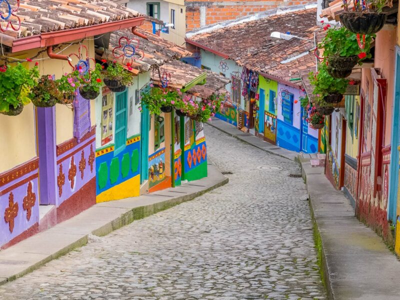 Narrow cobblestone street in Guatapé lined with brightly painted houses decorated with hanging flower baskets.