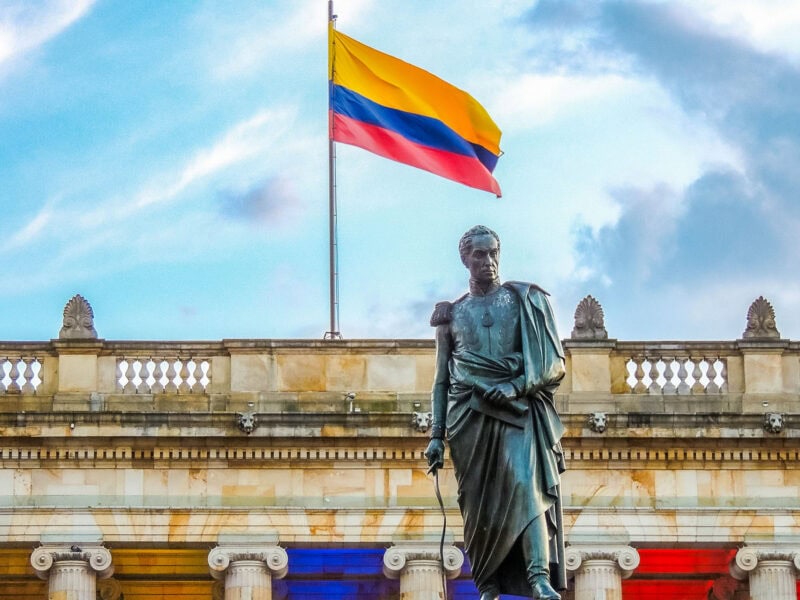 Statue of Simón Bolívar in front of a neoclassical building with the Colombian flag flying overhead